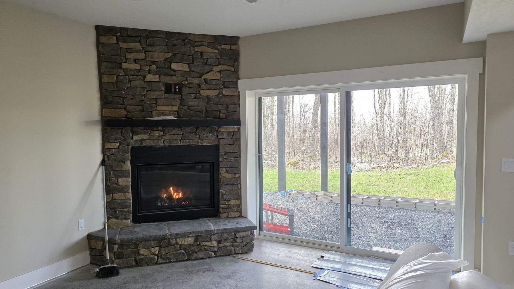 Stone fireplace beside a large sliding glass door with forest views