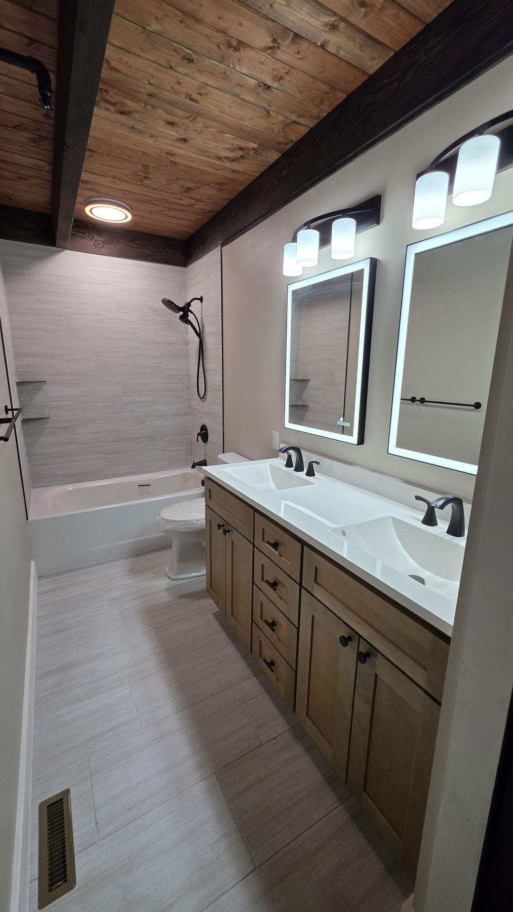 Modern bathroom with double vanity, backlit mirrors, and wood accents