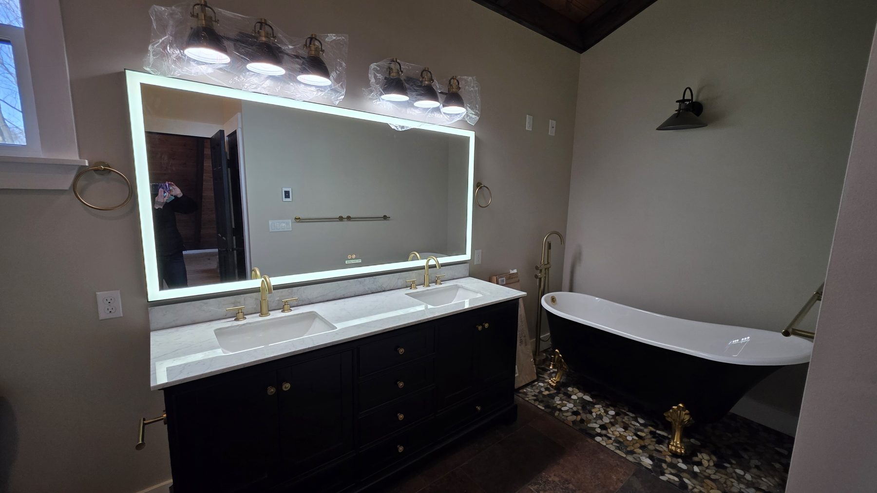 Primary bathroom with double vanity, illuminated mirror, and black soaking tub