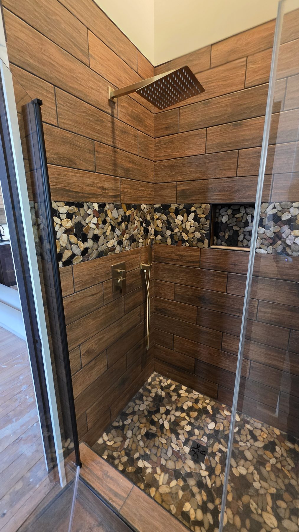 Walk-in shower with wood-look tile, pebble accents, and rainfall showerhead