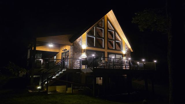 The house after dark, the gable lit from inside and string lights along the deck