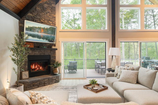 Fireplace lit, deck visible through the wall of gable windows. The forest is the