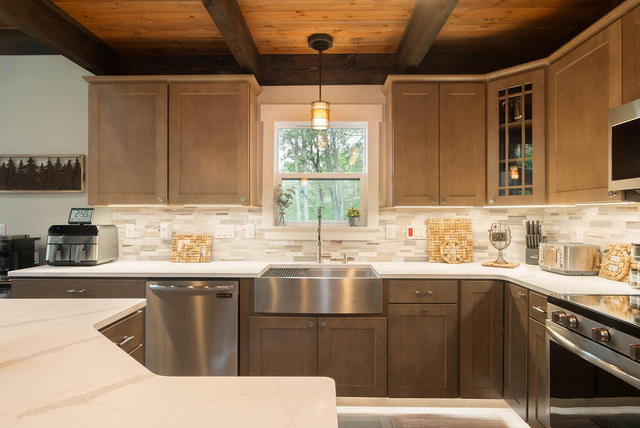 The farmhouse sink under the window, with the tile backsplash and the woods outs