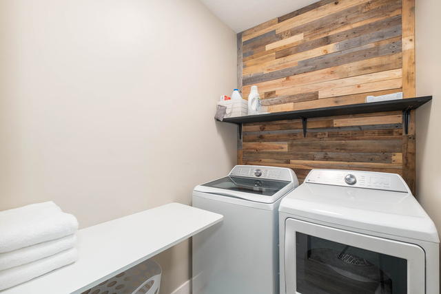 Full-size washer and dryer behind a reclaimed wood wall, with a folding counter 