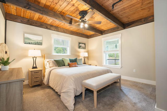 The main-floor king suite under wood-plank ceilings and beams, with a bench at t