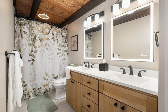 A main-floor full bath with a double vanity, two lit mirrors, and the heated til